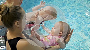 Swimming lesson. Mothers teaching to swim newborn baby at swimming pool