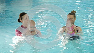 Swimming lesson. Mothers teaching to swim newborn baby at swimming pool