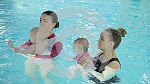 Swimming lesson. Mothers teaching to swim newborn baby at swimming pool