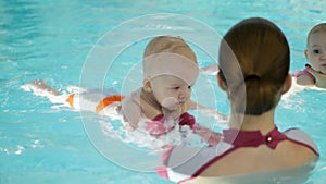 Swimming lesson. Mothers teaching to swim newborn baby at swimming pool