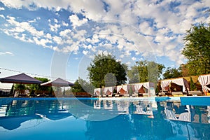 Swimming pool area with gazebos, deck chairs and sun umbrellas along the poolside in luxury resort. Summer houses