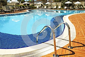 Swimming pool area of new luxury residential complex with tiles, chrome stairs handles and drains. Sunny beautiful day.