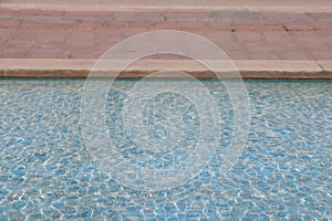 Swimming pool with blue water and brick wall background, shallow depth of field