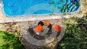 Swimming pool with blue water and sunbed deckchairs aerial top view, tropical vacation hotel resort