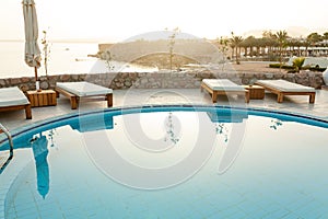 Swimming pool with chaise lounge and sunshade at tropical resort