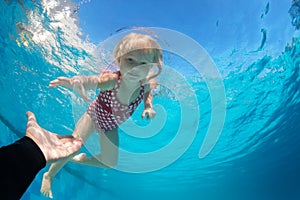 In swimming pool child dive underwater to reach extended hand