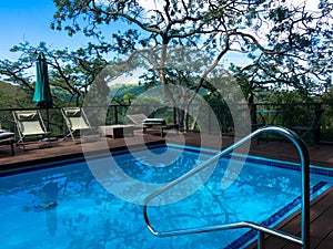 Swimming pool with deck chairs looking over the african wilderness in a luxury safari lodge. Relaxing vacation concept.