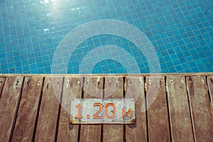 Swimming pool depth signs or markers located on wooden floor beside blue water pool.