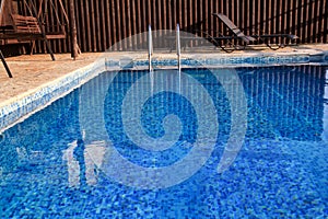 Swimming pool design modern architecture of luxury holiday villa. Relax near exotic swimming pool with handrail, deck chairs, sun