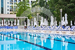 Swimming pool with empty loungers and closed umbrellas at luxury hotel