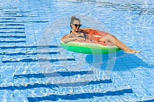 Swimming pool holidays. Happy young sexy girl in bikini swimsuit, sunglasses and inflatable rubber ring swimming in blue