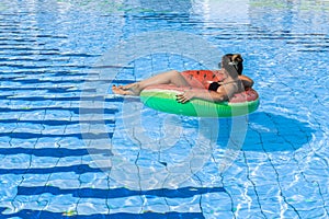 Swimming pool holidays. Happy young sexy girl in bikini swimsuit, sunglasses and inflatable rubber ring swimming in blue