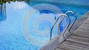 a swimming pool with limpid water having a hand railing on the edge