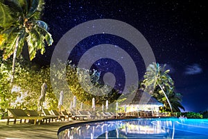 Swimming pool at night with palm trees and Milky Way sky view. Summer vacation, abstract relax background
