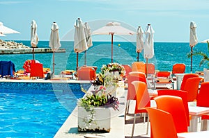 Swimming pool with red sun beds and umbrellas against an ocean
