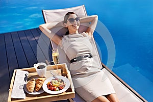 Swimming pool, relax and business woman with breakfast, holiday and summer with weekend break or nutrition. Person