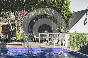 Swimming pool in a resort with terrace. Chairs and table on the patio. Blooming plants and flowers