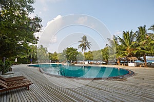 Swimming pool side of luxury hotel ith deck chairs, palm trees and blue ocean. Maldives