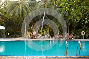 Swimming pool side of luxury hotel ith deck chairs, palm trees and blue ocean. Maldives