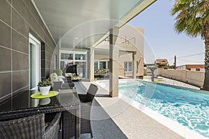 Swimming pool of a single-family house with a porch with dark wicker furniture