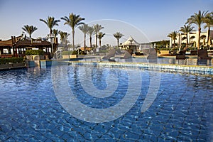 Swimming pool with the some beach lounges with a view on green palms