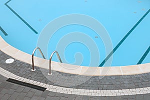 Swimming pool stone pavement tiles stone paving poolside background blue water surface. Ladder pool border. Edge pool