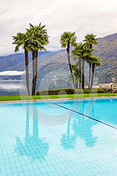 Swimming pool surrounded by palm trees and an Alpine Lake in Ascona in Switzerland