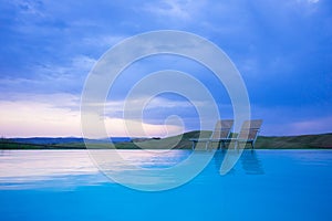 Swimming pool with two sun beds in evening light by sunset