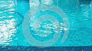 Swimming pool water surface with blue mosaic tiles. Beautiful background with texture of pool water with copy space. Nobody is in