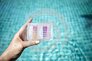 Swimming pool water testing test kit in girl hand over blurred blue water background