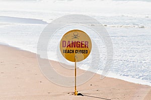 Swimming prohibited, beach closed warning sign on a beach with blue cloudy sky and sandy beach in background, room for text or cop