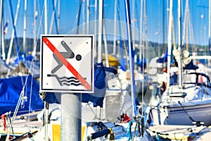 Swimming prohibited sign at marina harbor with sailboats in blurry background at lake Constance