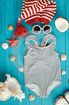 Swimsuit and Christmas hat next to beach accessories surrounded by seashells, starfish on the wooden turquoise background. Summer