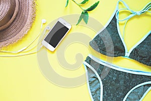 Swimwear in green color with smartphone and earphone flat lay on yellow