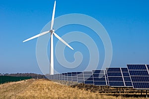 Wind turbine and solar panels in fields against blue sky producing renewable energy