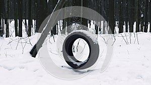 Swing in the forest, car tire hanging on a rope tied to a tree, winter background with homemade swing. Snowy forest