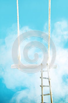 Swing with a ladder in the clouds on a blue background