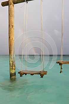 Swing in the ocean, rainbow in the sky after rain on a resort island in the Maldives