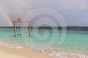 Swing in the ocean, rainbow in the sky after rain on a resort island in the Maldives