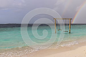 Swing in the ocean, rainbow in the sky after rain on a resort island in the Maldives