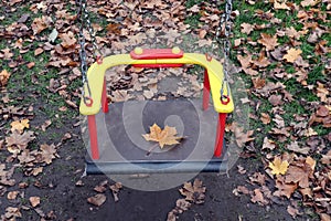 Swing on the Playground with a maple leaf, close - up-the concept of saying goodbye to autumn