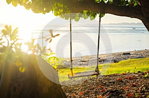 Swing on seashore during the sunrise. Sky and reflections on the water in the summer. Sun rays during the sunrise. Nusa Penida, Ba