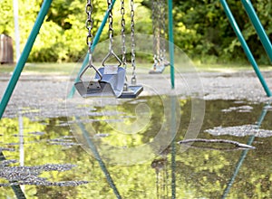 Swing set with puddle of water refecting the trees