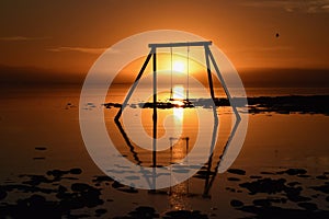 Swing set on the shoreline illuminated by a warm sunset