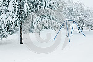 Swing set and trees in a park dusted and covered with fresh white snow