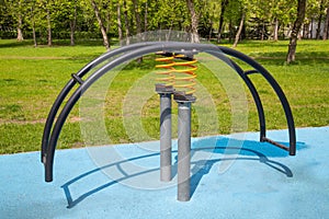 Swing on a yellow metal spring in the form of a curved arc on a playground with a rubberized surface. Kids sports