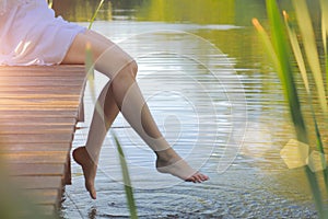 Swinging bare feet of woman sitting on pier. Summer vacation