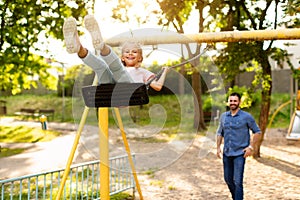 Swinging into happiness. Happy family having fun outside, father riding daughter on a swing, playing on playground