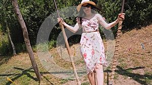 swinging. Happy young woman, in sunglasses and hat, having fun swinging on a big wooden swing, in the park, sunny summer