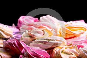 Swirls of sweet meringue on black background. Sweet meringue yellow, pink and purple color in confectionery. Sweet